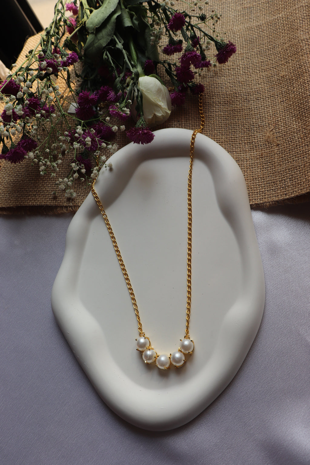 Pearl necklace on a white dish with flowers in the background