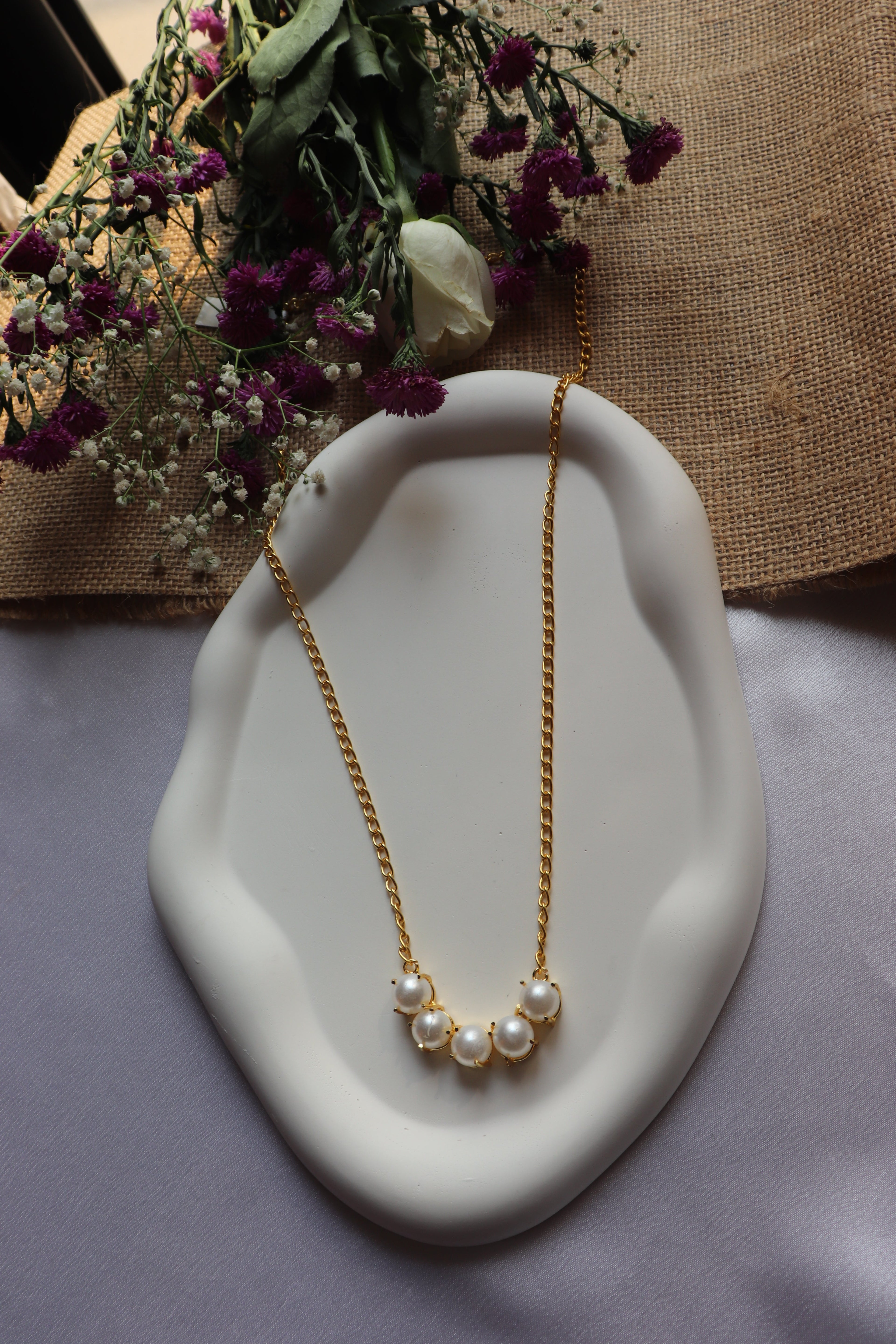 Pearl necklace on a white dish with flowers in the background
